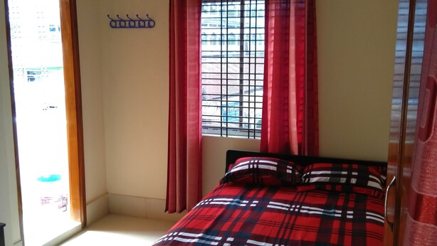 Une chambre à coucher avec un lit, un appareil de climatisation, une fenêtre avec des rideaux rouges et une vue sur les bâtiments environnants.