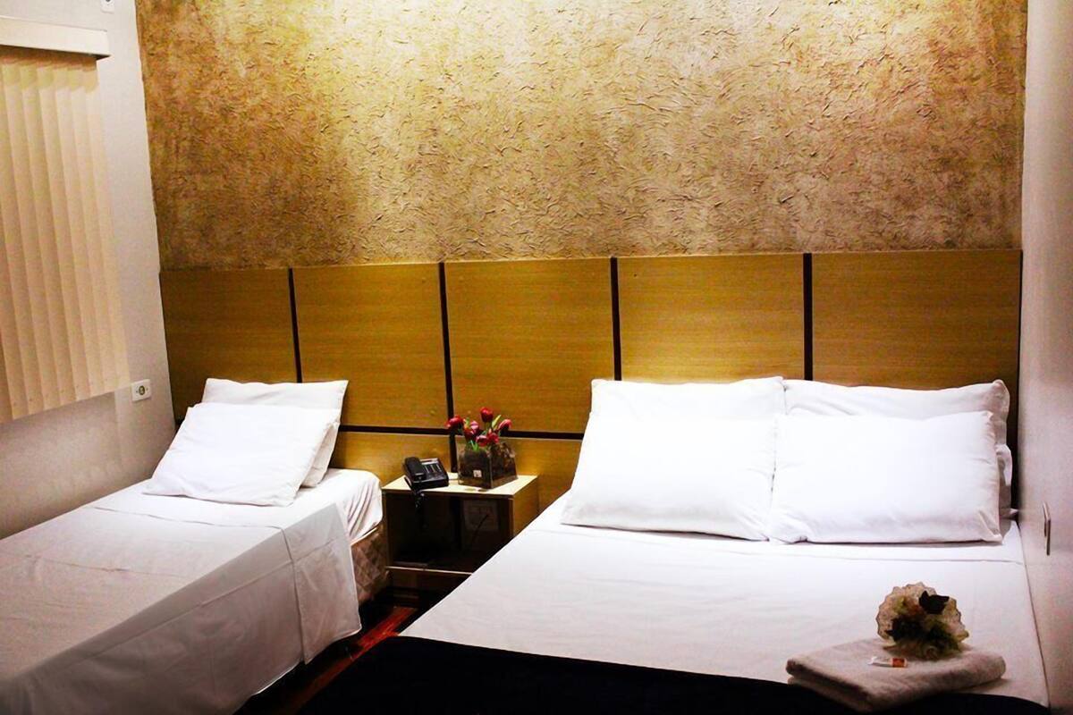 A hotel room with two single beds, a wooden headboard, a nightstand with a phone and a vase of flowers, and a small table with a decorative item.