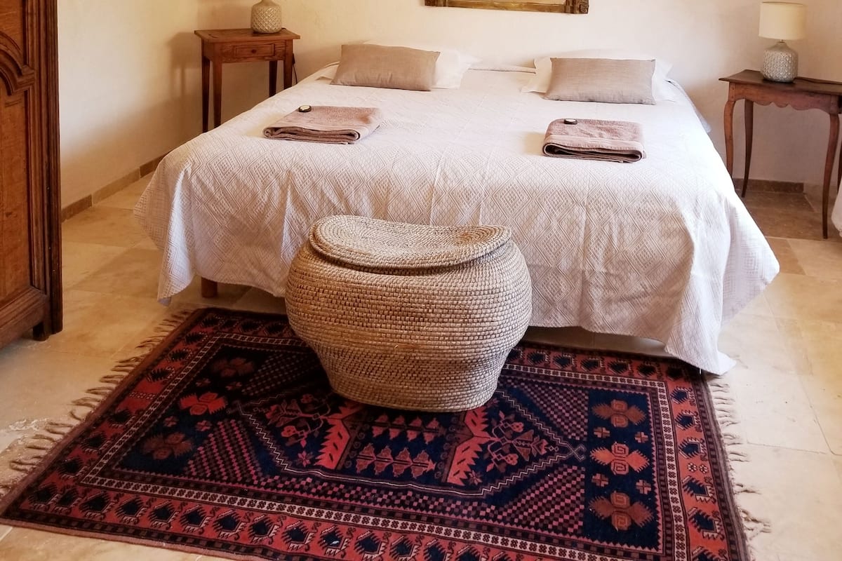 A bedroom with a bed, a large mirror, a bedside table, a lamp, a rug, and a wooden door.