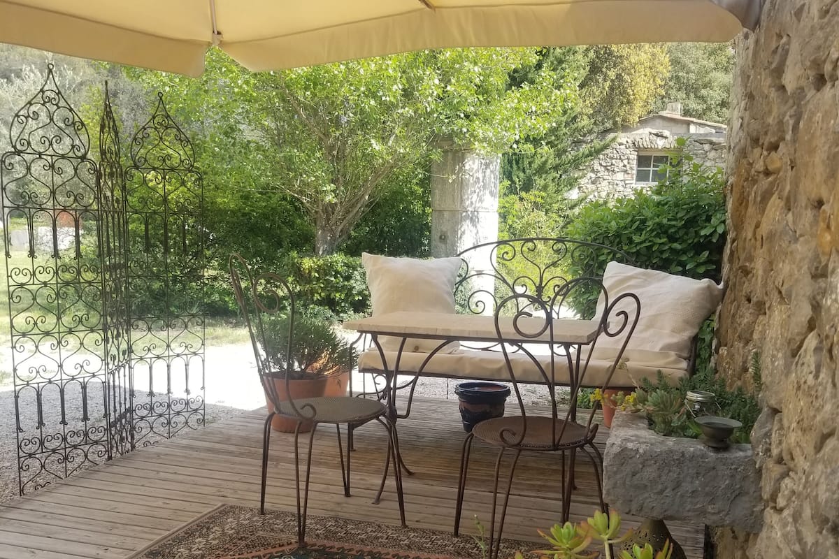An outdoor seating area with a table and chairs under a canopy, surrounded by potted plants and a decorative metal fence.