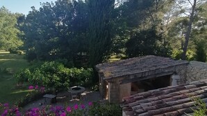 A garden with a stone building, surrounded by trees and vibrant flowers. - Le Mas des Escans (Le Beausset)