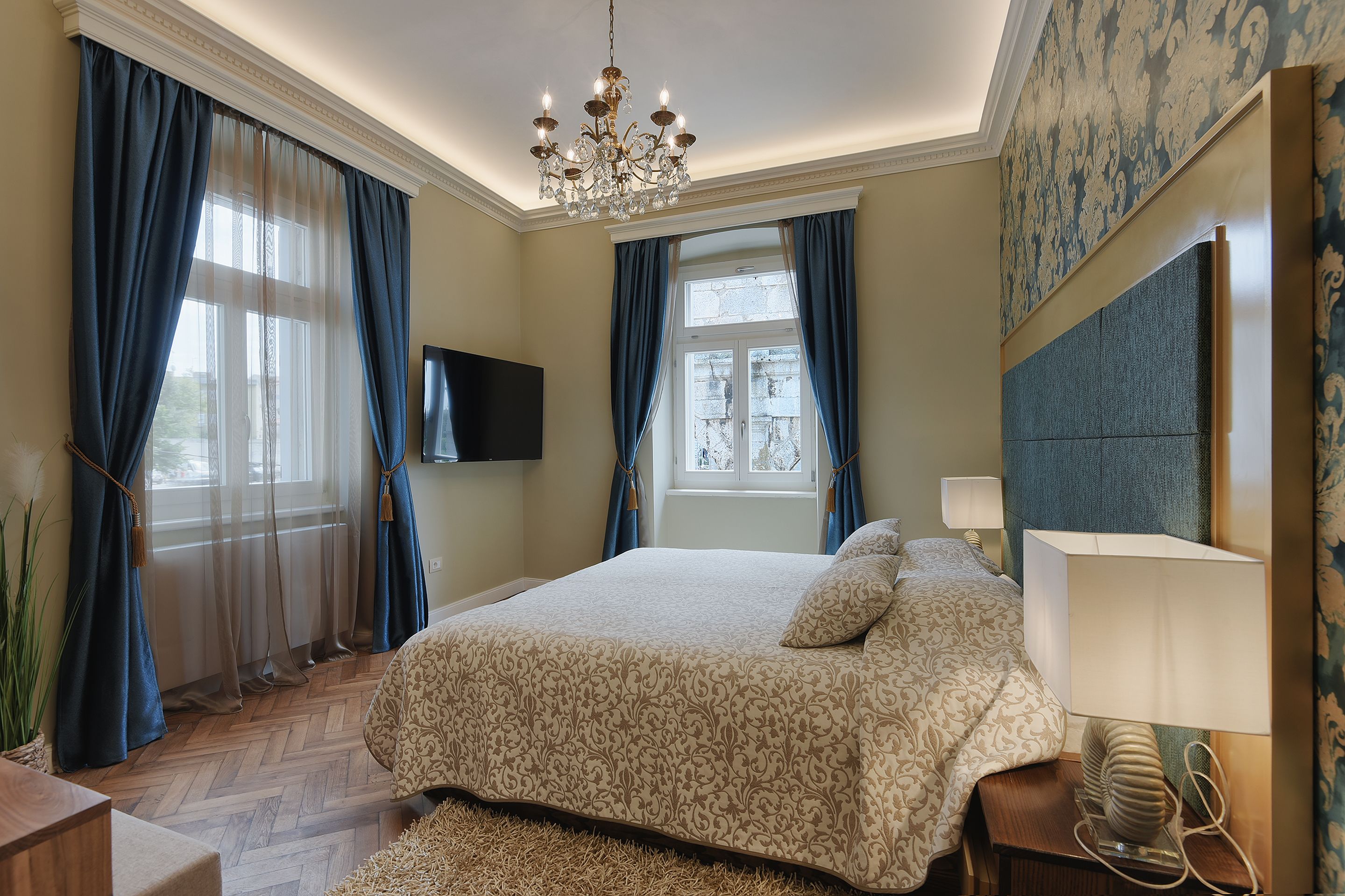 Quarto de hotel com uma cama grande, um candelabro, uma televisão e vista para o exterior.