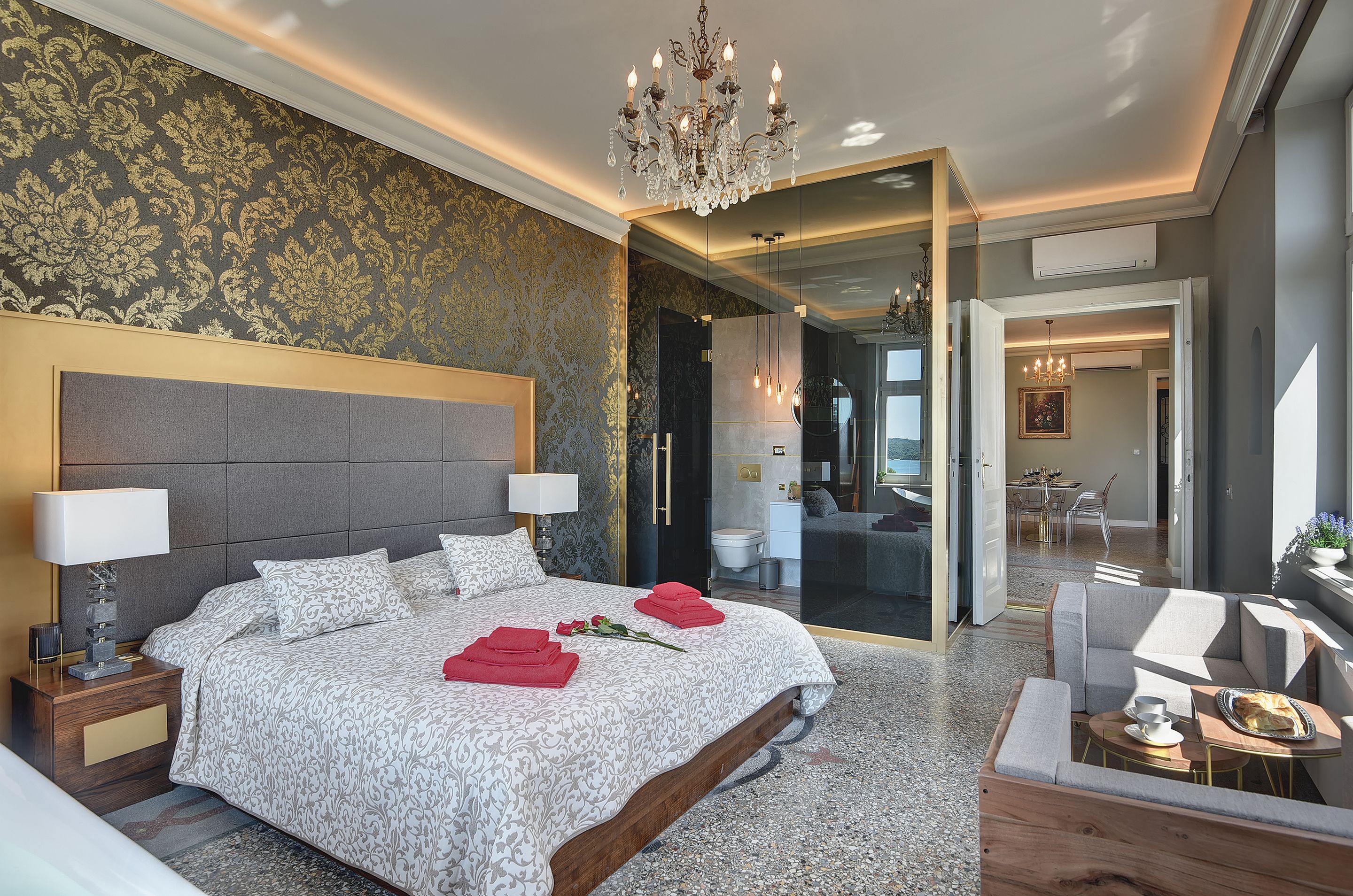 Ein geräumiges Schlafzimmer mit einem großen Bett, einer Kandelaber und einem modernen Badezimmer, das durch eine offene Tür zu sehen ist.