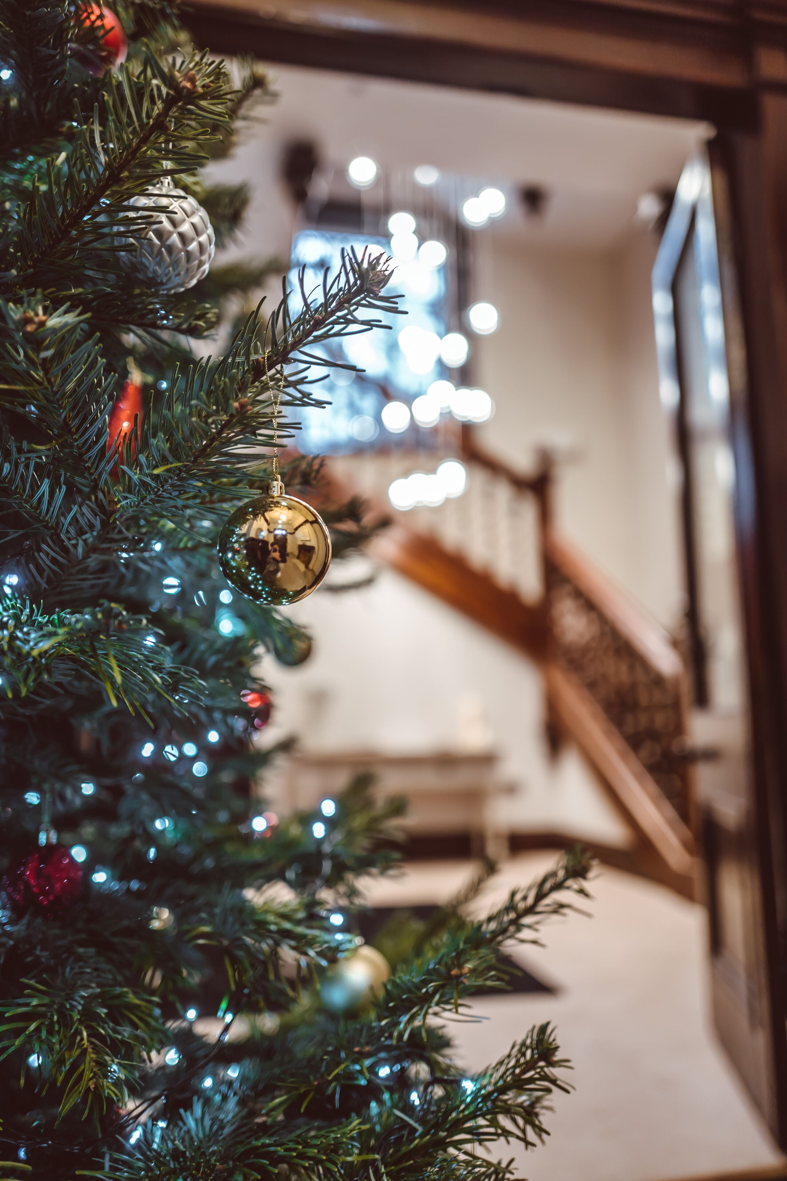 A Christmas tree with ornaments and lights, a staircase, and a railing in the background.