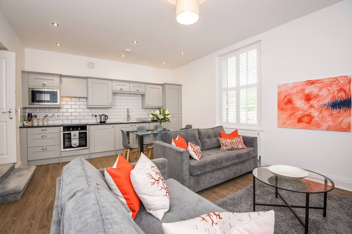 A modern kitchen with grey cabinets, a microwave, and a dining area with a glass table.