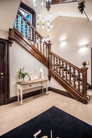 A wooden staircase with a dark finish, a white console table with a vase of flowers, and a dark blue rug on the floor. - 52 Old Elvet (Durham)