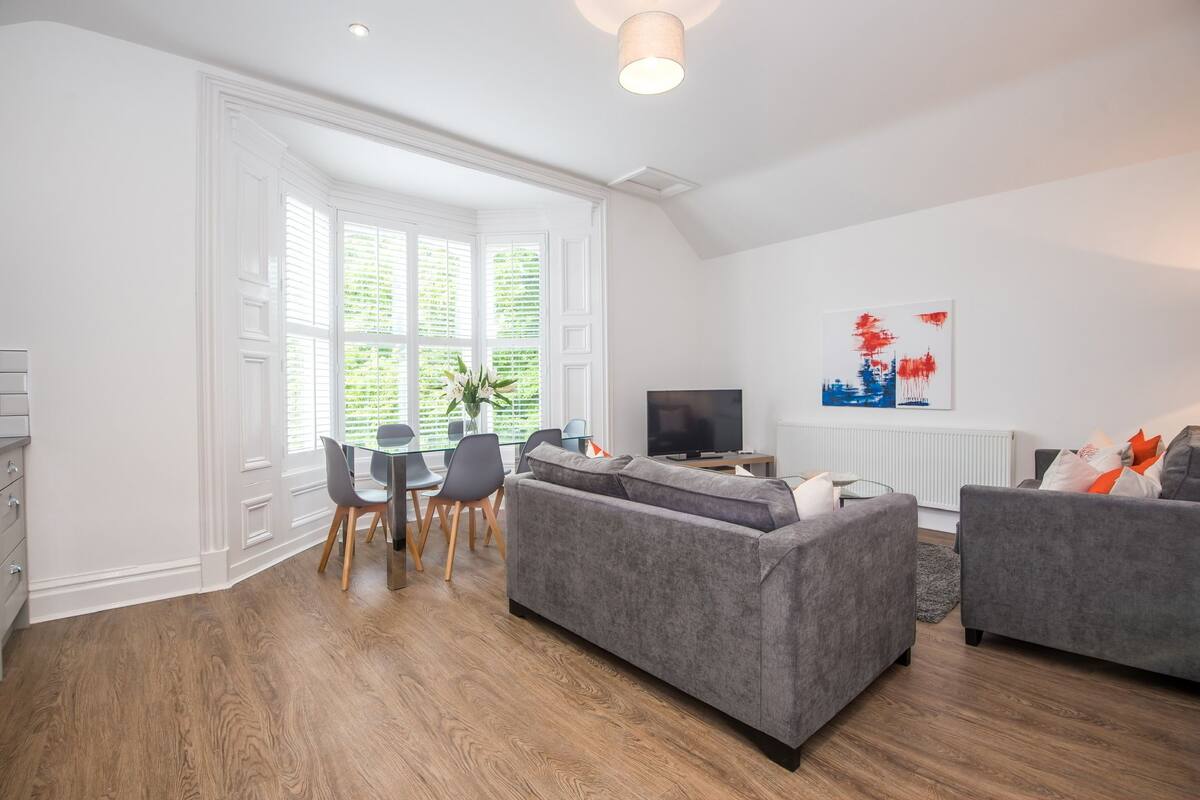 A modern living room with a dining area, grey sofas, and a TV.