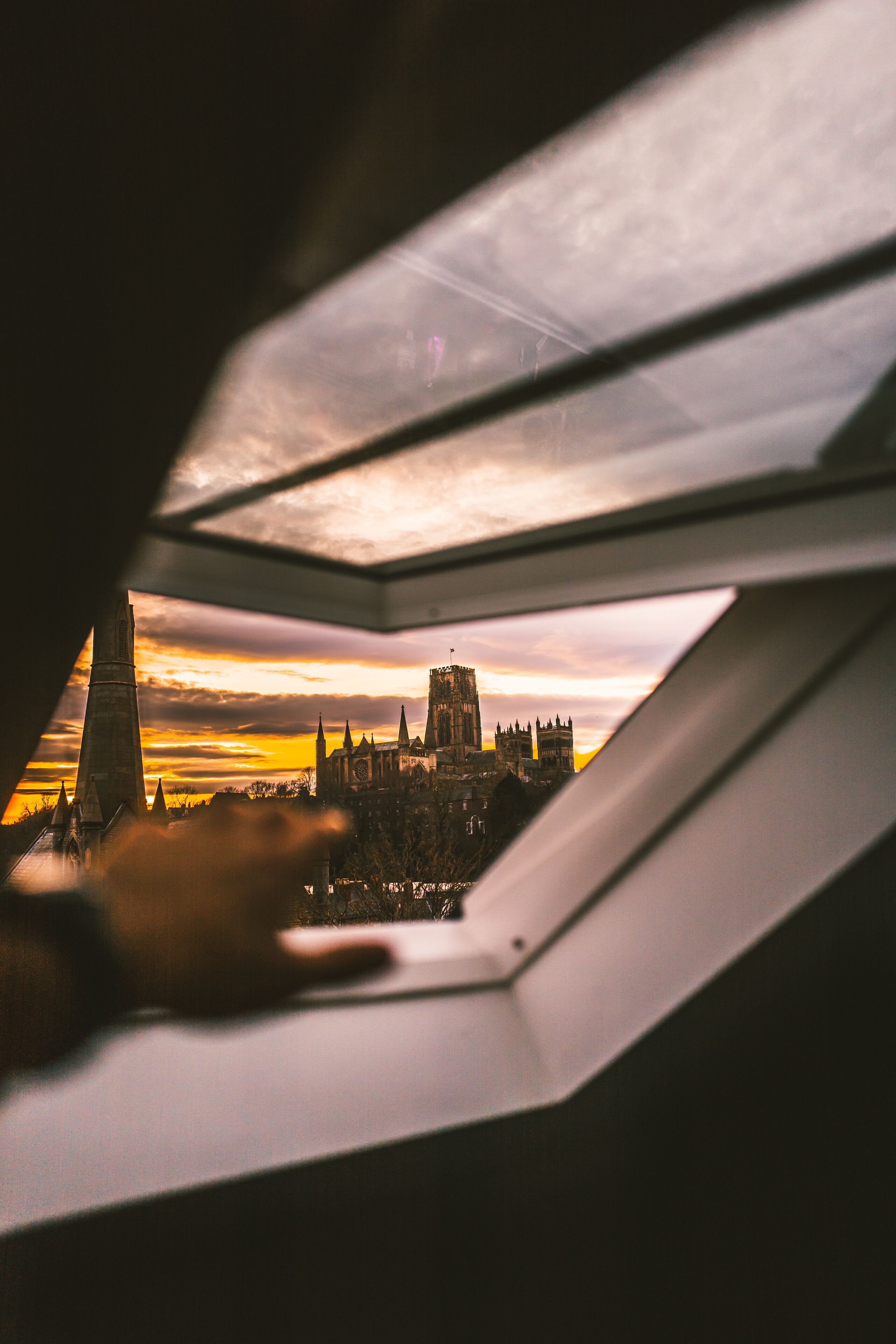 Une vue à travers une fenêtre sur un paysage urbain au coucher du soleil, avec notamment une église imposante et des flèches.