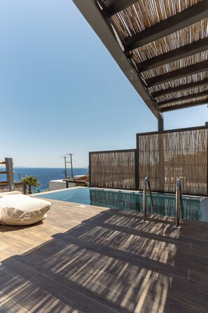 A pool area with a view of the sea, wooden deck, and a covered seating area. - Maregold Mykonos Micro-Suites, Adults Only (Mykonos)