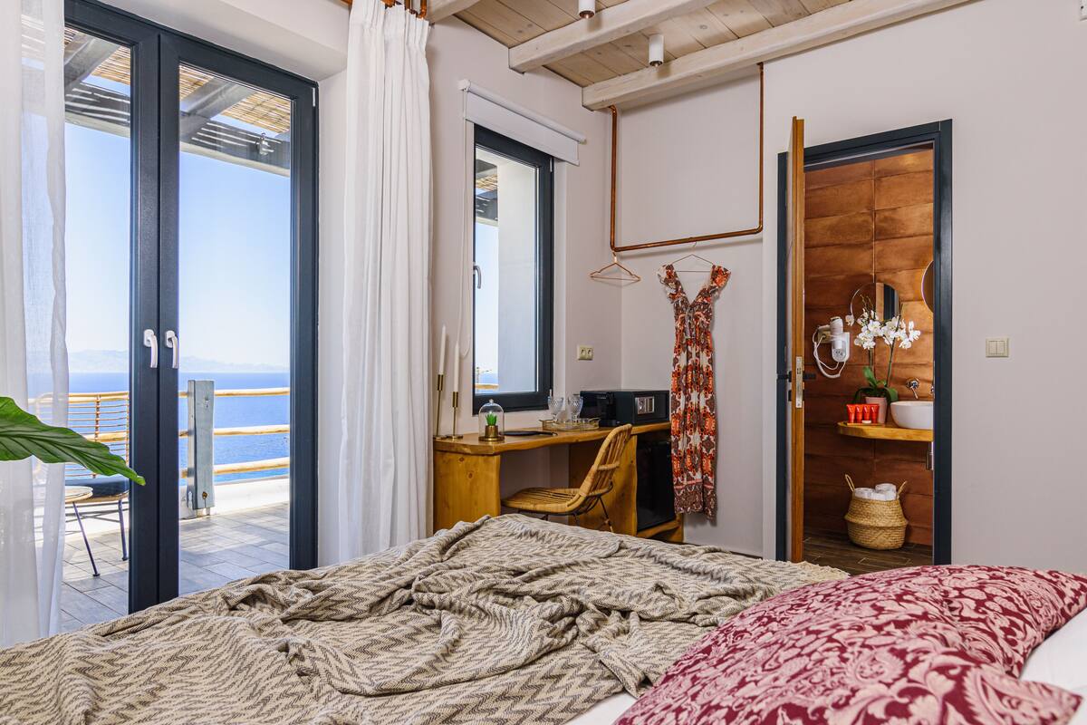 Un dormitorio con cama, escritorio y silla. Se ve el mar a través de una puerta corrediza.