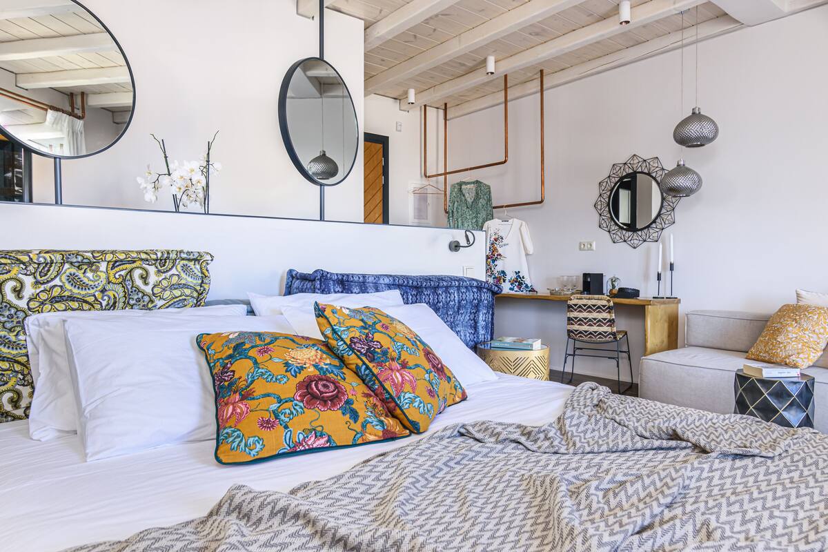 Un dormitorio con cama, dos almohadas, cómoda, silla, escritorio y dos espejos.