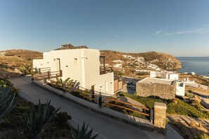 A coastal property with a white building, a paved walkway, and a view of the sea and hills. - Maregold Mykonos Micro-Suites, Adults Only (Mykonos)