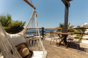 A hammock, a wooden table, and chairs on a deck with a view of the sea. - Maregold Mykonos Micro-Suites, Adults Only (Mykonos)