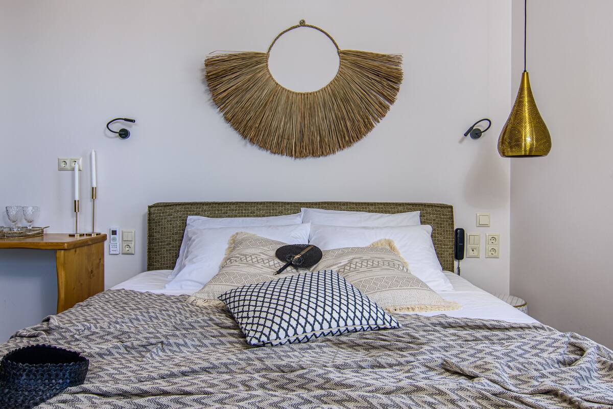 Una cama bien tendida con ropa de cama estampada, una obra de arte tejida en la pared, lámparas de noche y un teléfono junto a la cama.