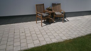 An outdoor seating area with two wooden chairs and a small table, set against a white wall with a dark baseboard. - Wohnen im ehemaligen Kaminstudio (Lutherstadt Wittenberg)
