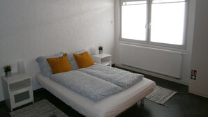 A bedroom with a bed, two nightstands, a window, and a radiator. - Wohnen im ehemaligen Kaminstudio (Lutherstadt Wittenberg)