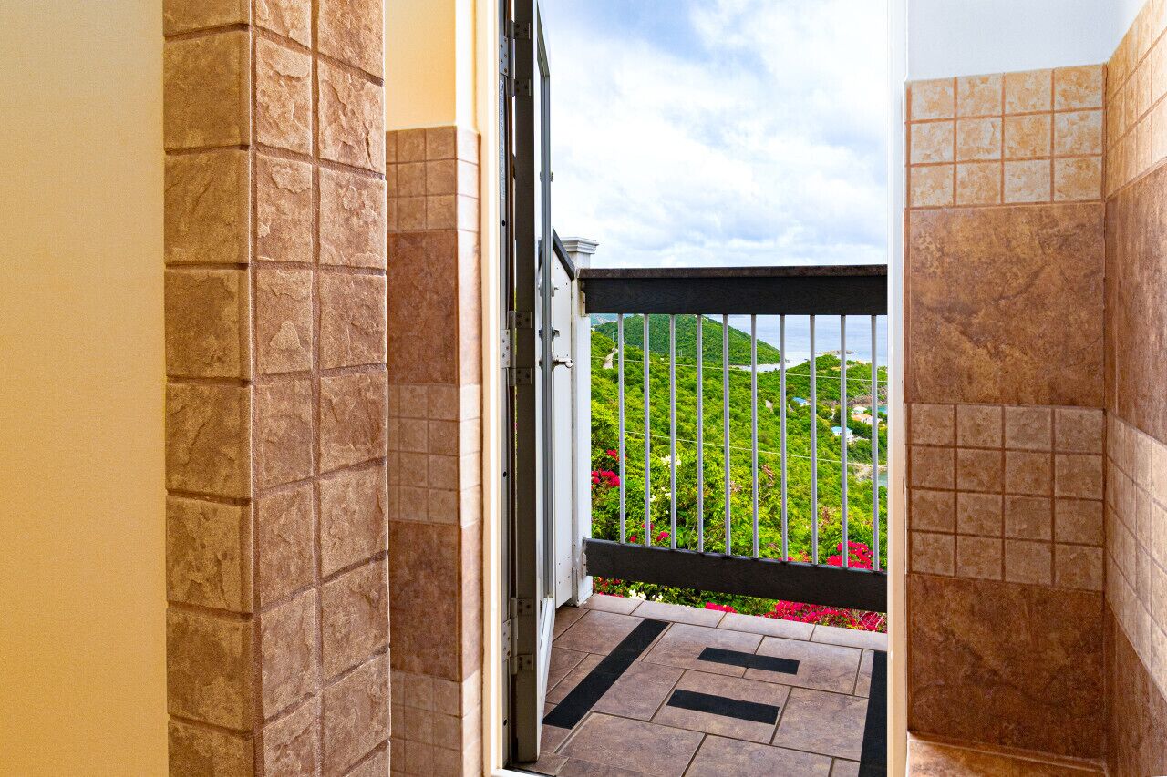 A doorway leading to a balcony with a view of a landscaped garden and hills.