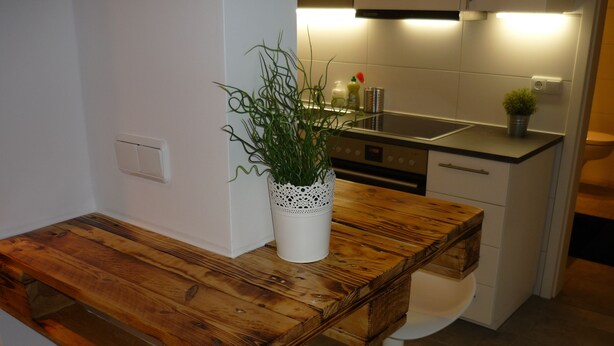 Una cocina con un banco de madera, una planta en maceta y electrodomésticos modernos.