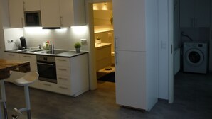 Una cocina moderna con armarios blancos, horno empotrado y un lavamanos. Hay un taburete de bar y una pequeña planta en maceta sobre la encimera.