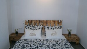 Una cama con cabecera de madera, dos mesitas de noche con plantas en macetas y una lámpara de pared.