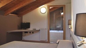 Un dormitorio con techo de madera, una cama, un televisor y una ventana con persianas.