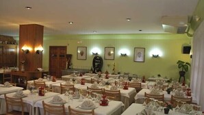 Un restaurante con varias mesas dispuestas para comer, sillas de madera y una pared verde con cuadros enmarcados.