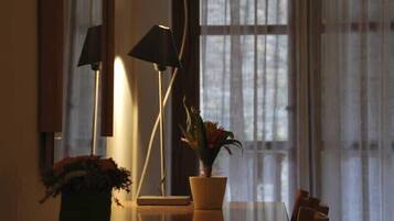 Une pièce comprenant un bureau, une plante en pot, une lampe et une fenêtre ornée de rideaux légers.