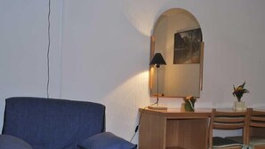 Una habitación con un sillón azul, un escritorio de madera con una lámpara, un espejo y una silla.