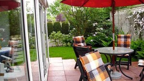 An outdoor patio with a glass door, a round table, and two chairs with plaid cushions. - Hotel Pension Petra (Bad Zwischenahn)