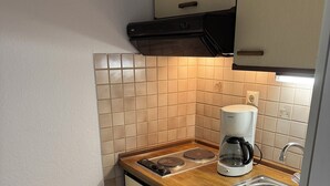 A compact kitchen with a built-in stove, a coffee maker, and a sink. - Hotel Pension Petra (Bad Zwischenahn)