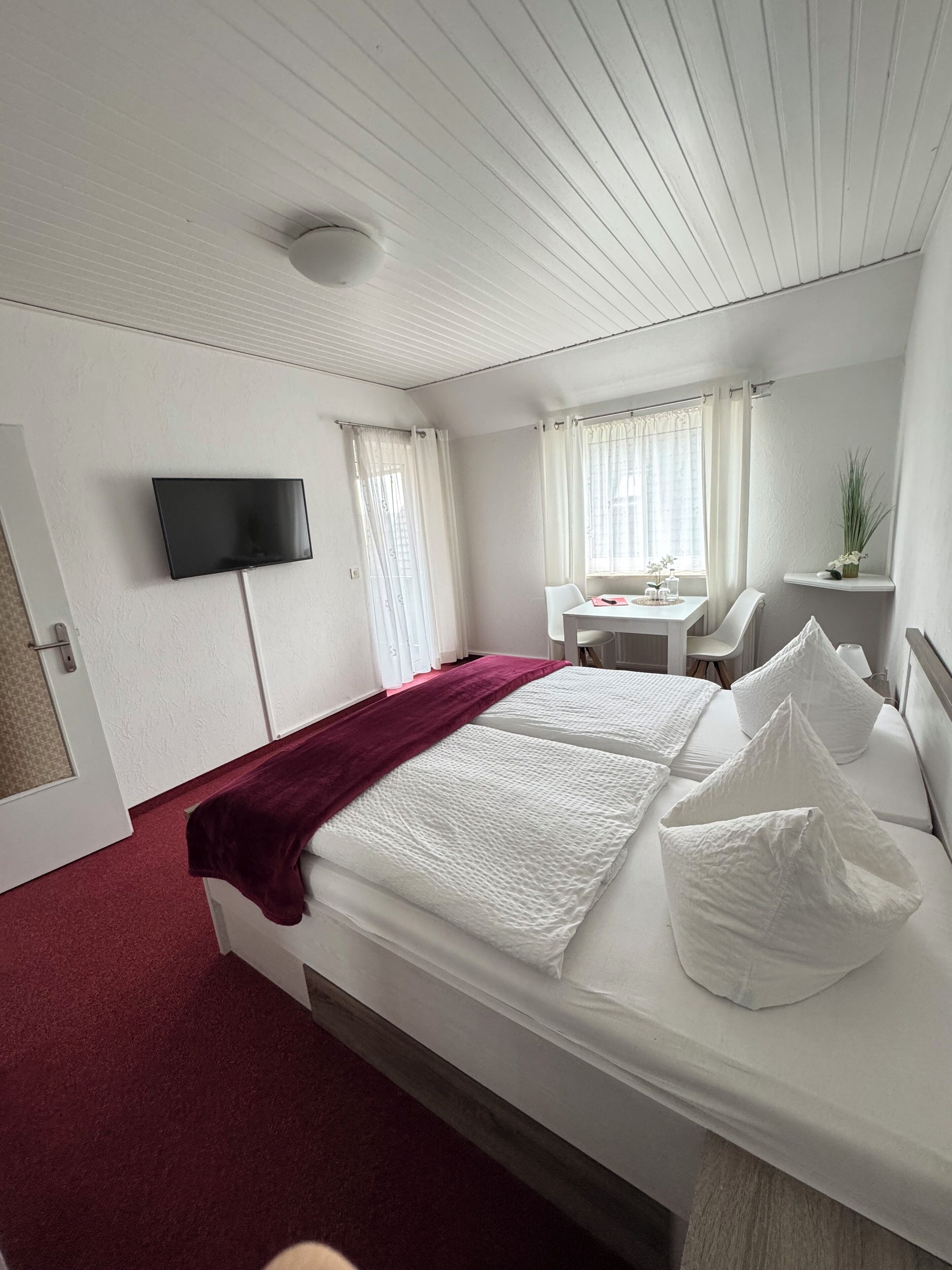 A hotel room with a bed, a desk, a chair, a TV, and a window with curtains.