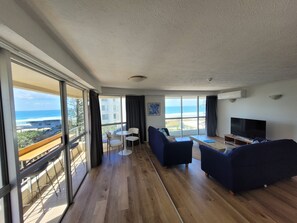Ein geräumiges Wohnzimmer mit großem Fernseher, bequemen Sitzmöglichkeiten und einem Balkon mit Meerblick.