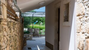 A stone corridor leading to an outdoor patio area with wicker furniture and a blue umbrella. - Traditional holiday house in peaceful location, village Rakalj (Rakalj)