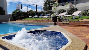 En swimmingpool med ett bubbelbad, solstolar och en skylt som visar att det finns lediga platser.