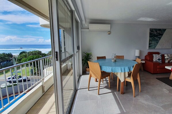 Uma varanda com mesa e cadeiras, um sofá vermelho e vista para o mar.