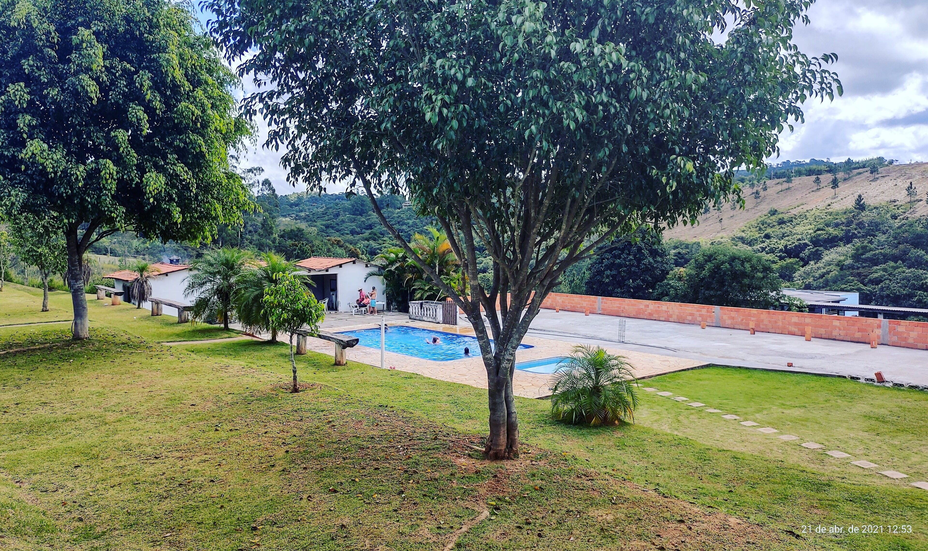 Une piscine entourée d’une zone herbeuse avec des arbres, un petit bâtiment et, au loin, un paysage vallonné.