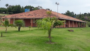 A single-story building with a red-tiled roof, surrounded by a grassy lawn and palm trees.