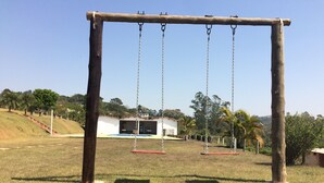 A wooden swing set in a grassy area with a building in the background.