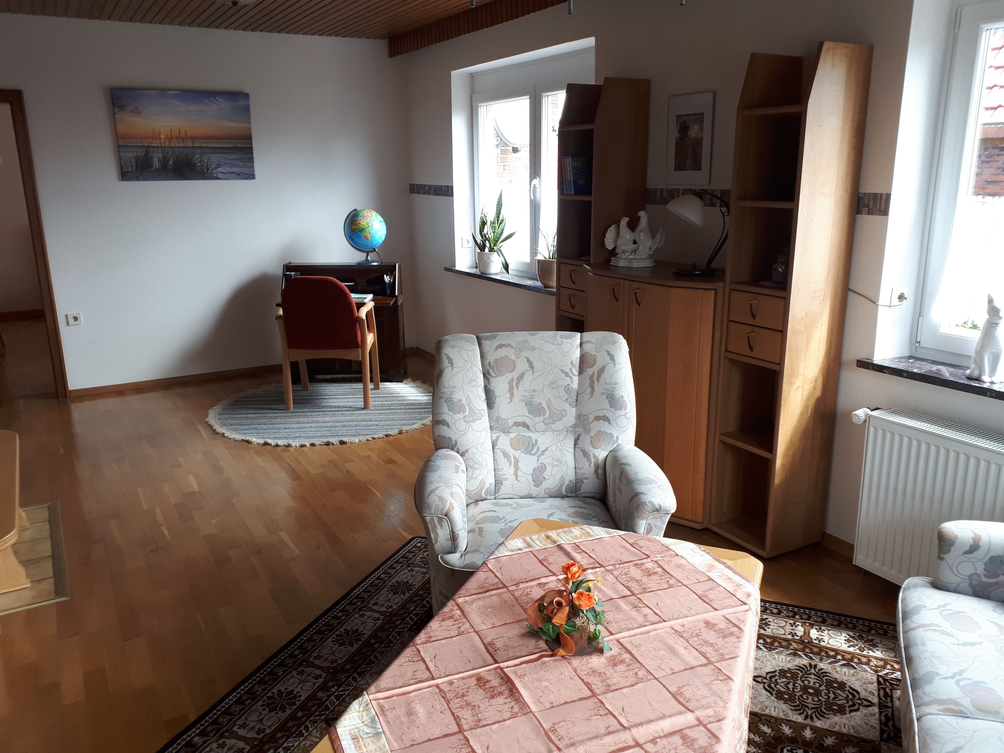 En stue med en sofa, et sofabord med en dekorativ genstand, en globus på et skrivebord og en reol.