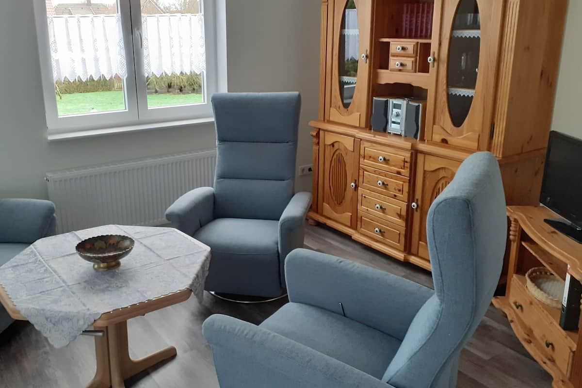 A living room with two blue armchairs, a small table with a bowl, and a wooden cabinet with drawers and shelves.