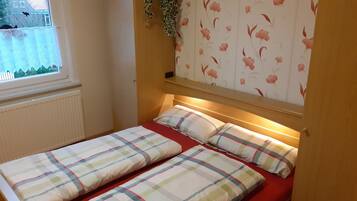 A small, cozy bedroom with a single bed, floral wallpaper, and a window with a view.