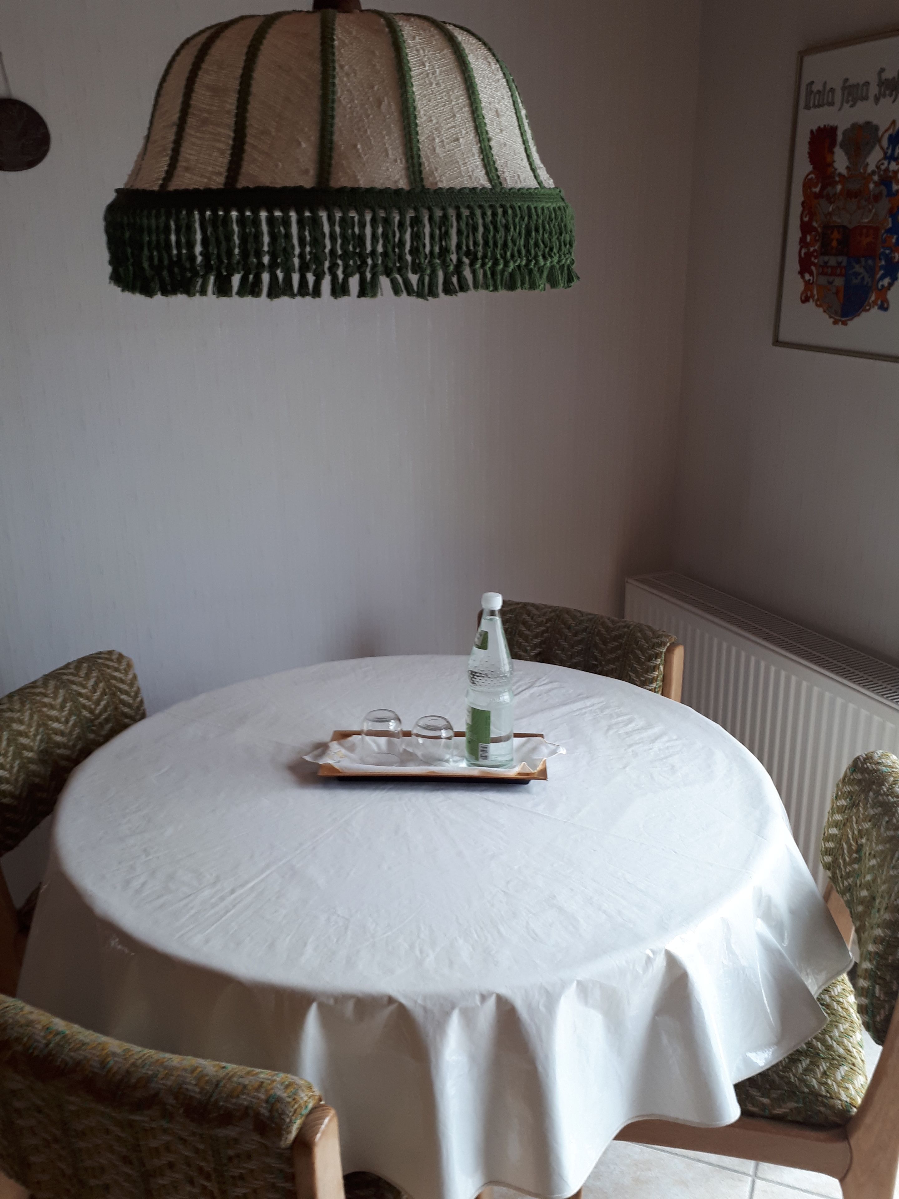 Una mesa redonda de comedor con mantel blanco, rodeada por cuatro sillas estampadas. Una bandeja con una botella y vasos está colocada sobre la mesa.
