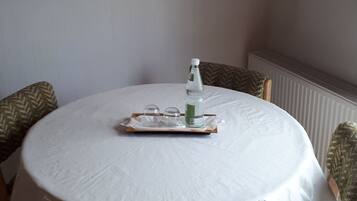 Una mesa redonda de comedor con mantel blanco, rodeada por cuatro sillas estampadas. Una bandeja con una botella y vasos está colocada sobre la mesa.