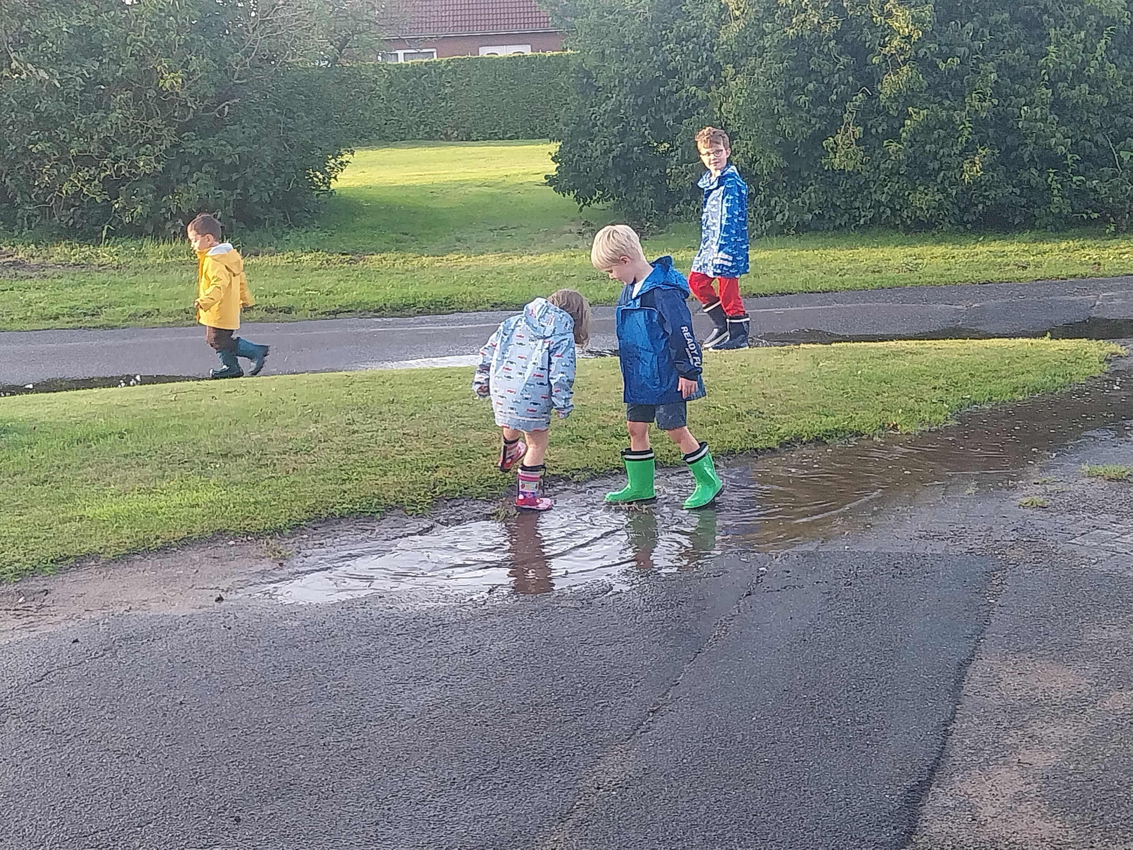 Een groep kinderen speelt in een plas water op een nat wegdek.