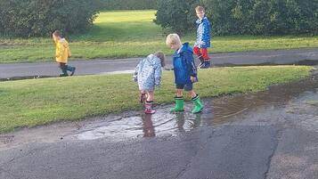 Een groep kinderen speelt in een plas water op een nat wegdek.