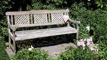 A wooden bench in a garden with dense foliage and flowers.
