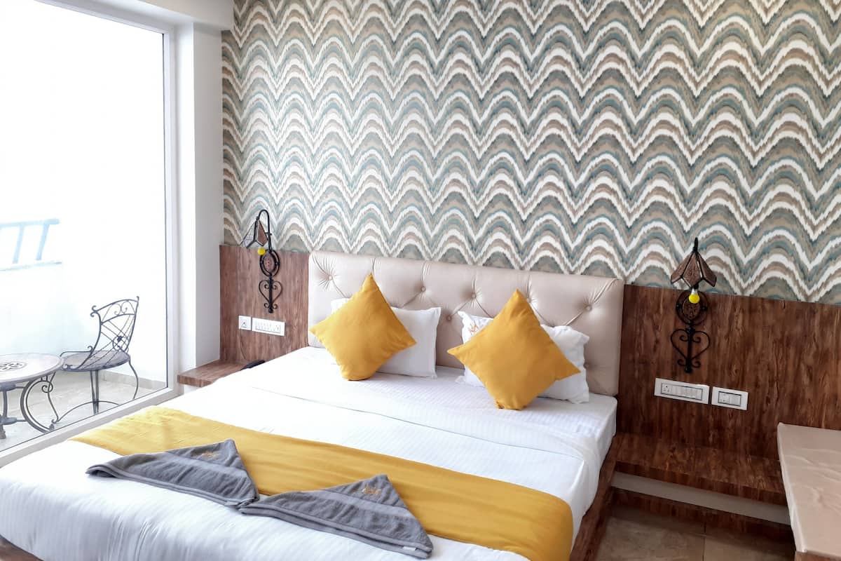 A hotel room with a large bed, two yellow pillows, a grey throw blanket, and a patterned wallpaper.