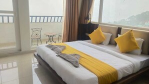 Un cuarto de hotel con una cama grande, un balcón con una silla y vistas a la ciudad.