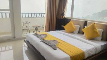 A hotel room with a large bed, a balcony with a chair, and a view of the city.