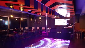 Un interior moderno con una pista de baile iluminada con luces LED, mesas, sillas y una pantalla grande.
